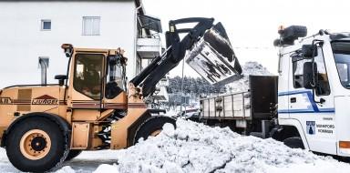 Effektiv snöplogning: en gul traktorgrävare lastar upp snö på en vit lastbils flak för bortforsling av snön.